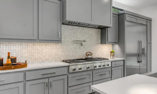 Modern kitchen with gray cabinets, stainless steel appliances, and a tiled backsplash.