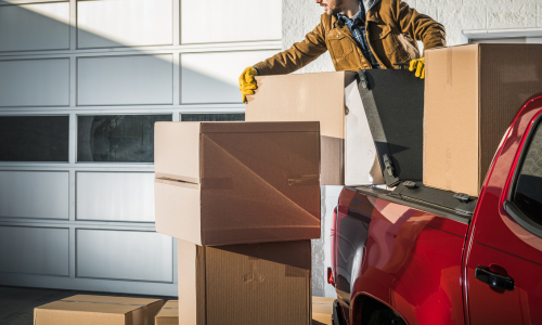 A farmer loading a truck bed with large cardboard boxes.